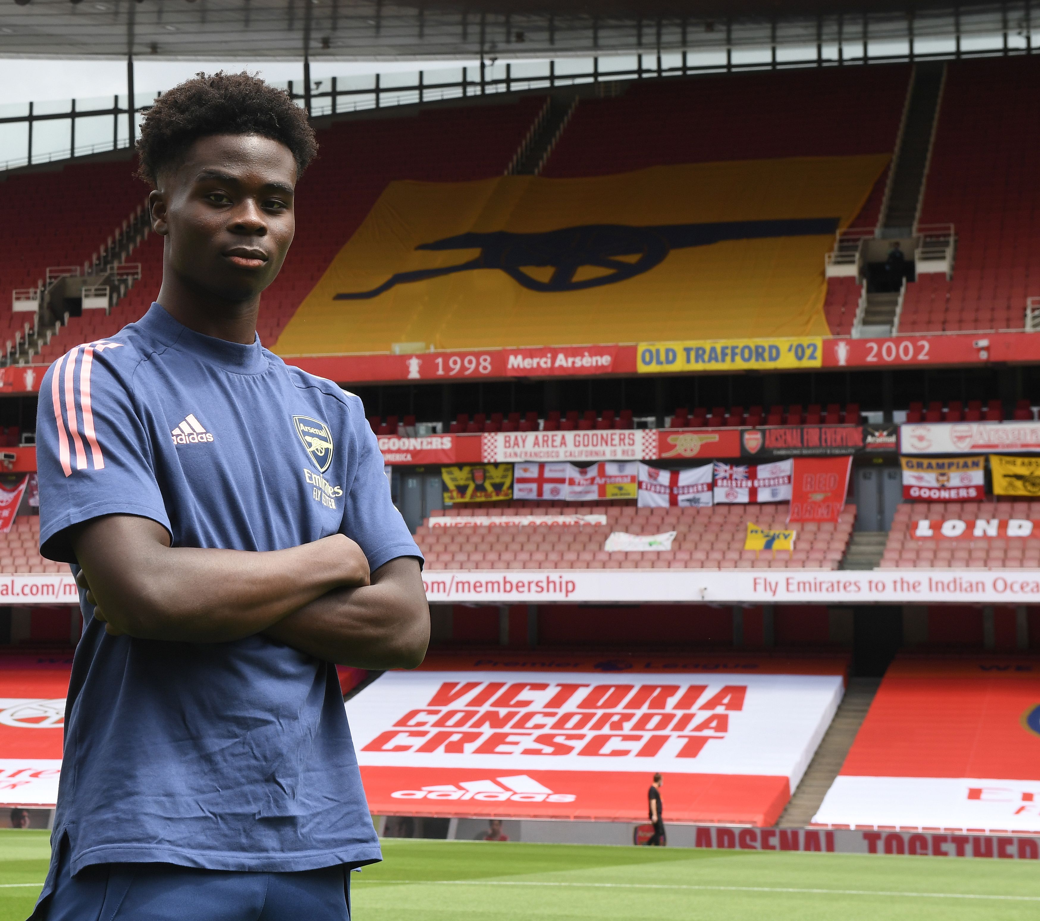 Bukayo Saka poses with his arms folded on the pitch at Emirates Stadium after signing a new contract in 2020